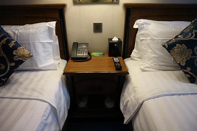 ベットの間に室内電話やリモコン、スリッパが置かれています。