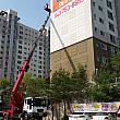 韓国は一軒屋が少なく、高層住宅が多い国。たまたま通りかかった場所でマンションの壁に貼る作業をしていますが