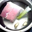 ２．鍋に湯を沸かし、つぶした生姜（またはニンニク）、葱の白い部分、塩少々と豚肉を入れてゆでます。火が通ればとり出して氷水につけて冷まし、薄切りにします。